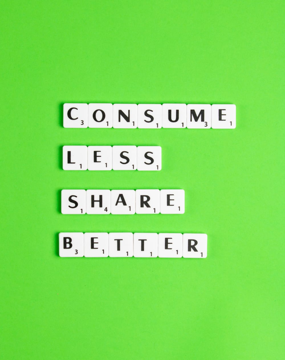 Scrabbleletters op een groene ondergrond vormen de woorden consume less, share better